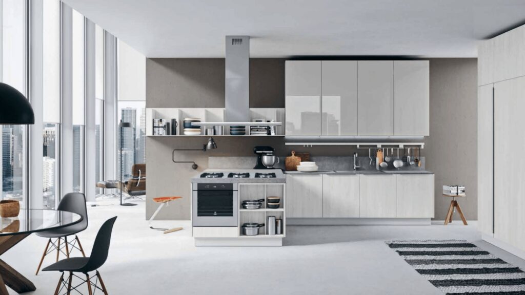 Cocina moderna con mobiliario blanco y gris claro, abierta a un salón con ventanales y vistas urbanas.