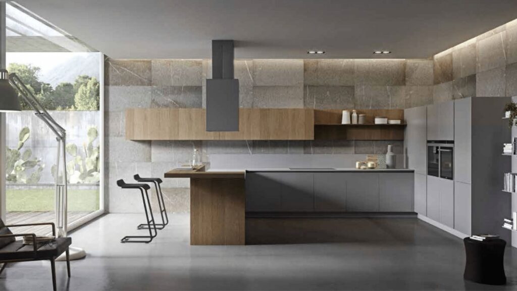 Cocina moderna con isla central en madera y mobiliario gris mate, integrada en un espacio luminoso con pared de piedra y vistas al jardín.